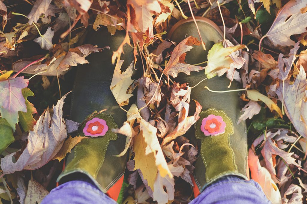 Overhead shot of a girl's rubber boots among fallen leaves.