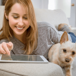 Young lady happily interacting with her tablet while holding a puppy.