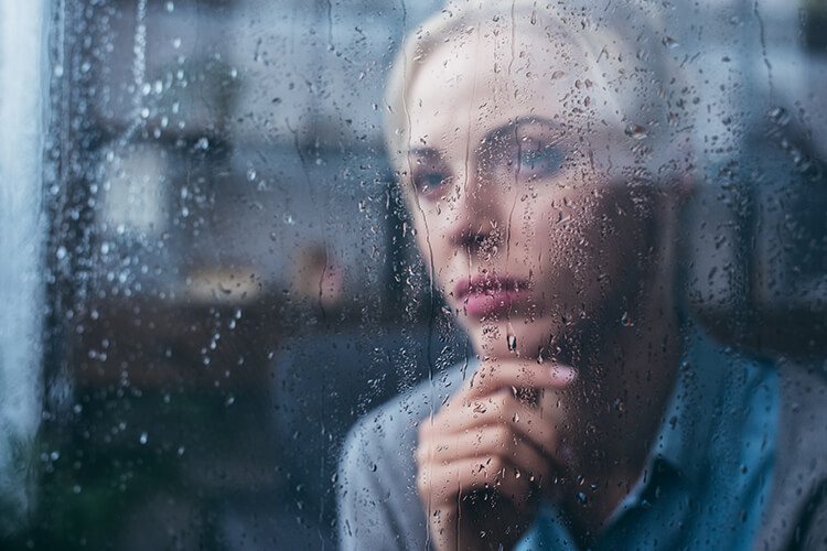 Sad woman looking out of a rain-soaked window