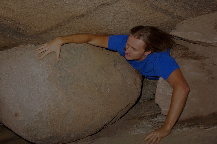 man crawling through a very small cave opening