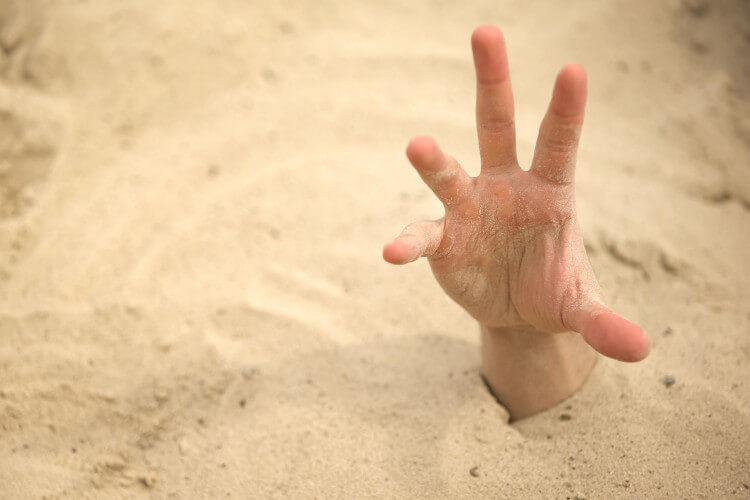 hand reaching out from beneath sand